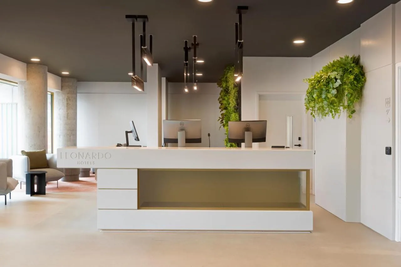 an office lobby with a white reception desk with plants at Leonardo Hotel Manchester Piccadilly in Manchester